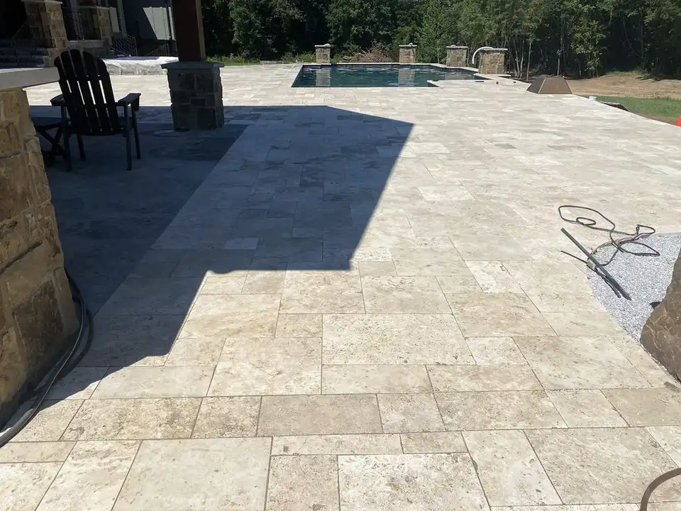 Travertine pool deck around a pool with stone pillars at the far end, one of our jobs