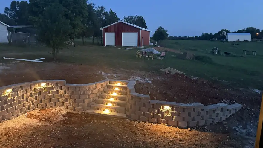 A lit segmental block retaining wall with built-in steps by Ozarks Custom Hardscaping